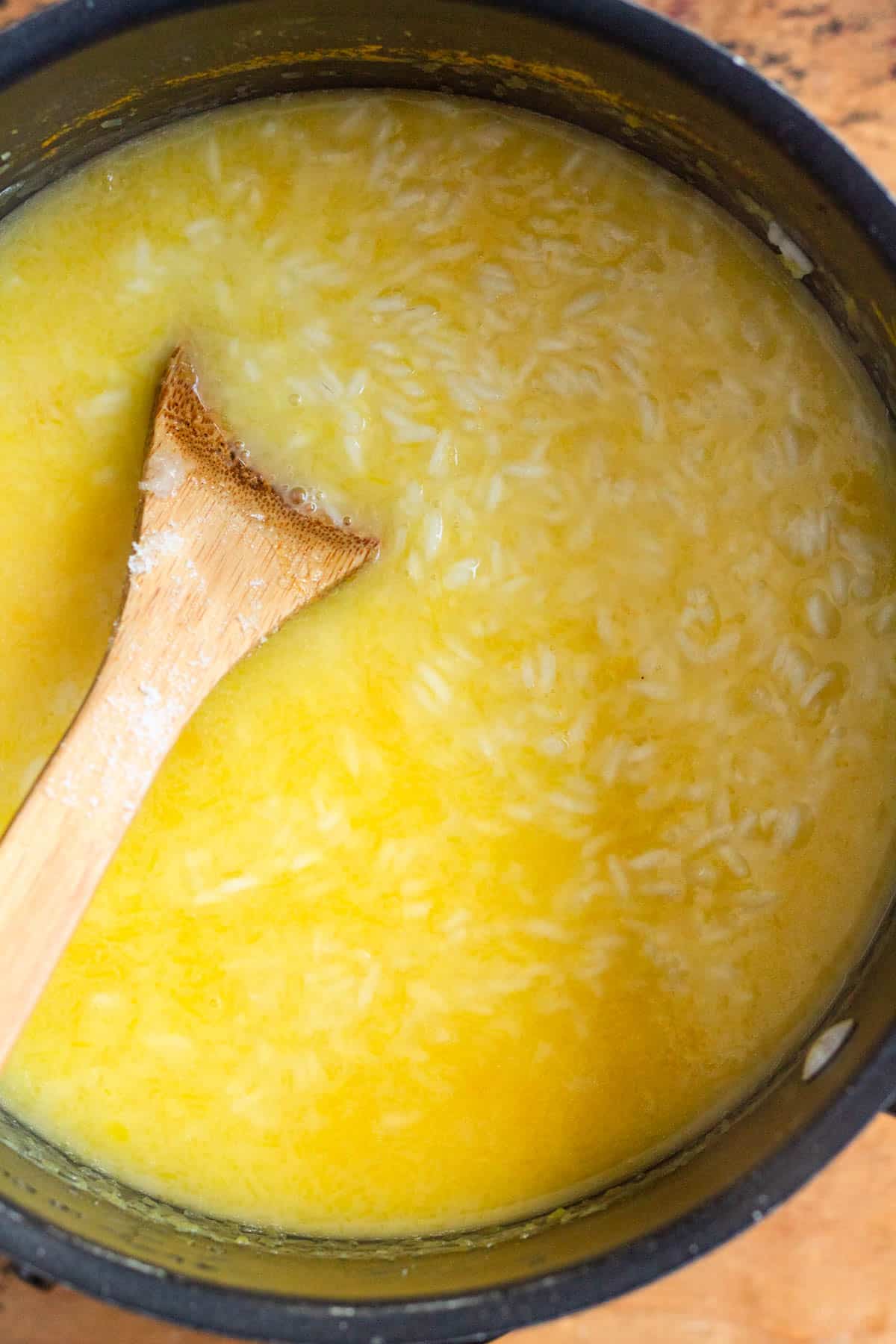 Pumpkin purée and coconut cream being stirred together in a pot of rice.