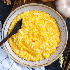 A creamy bowl of bright yellow pumpkin rice served in a rustic dis