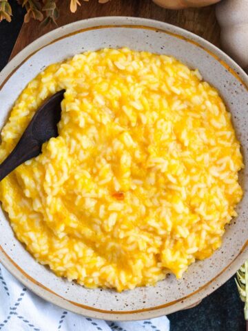 A creamy bowl of bright yellow pumpkin rice served in a rustic dis