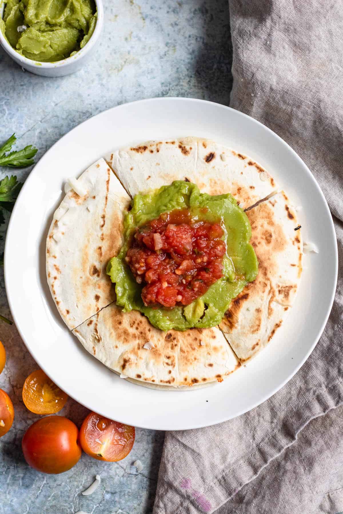 Top image of Sincronizadas cut into fours and topped with guacamole and salsa with cherry tomatoes laying next to the plate.