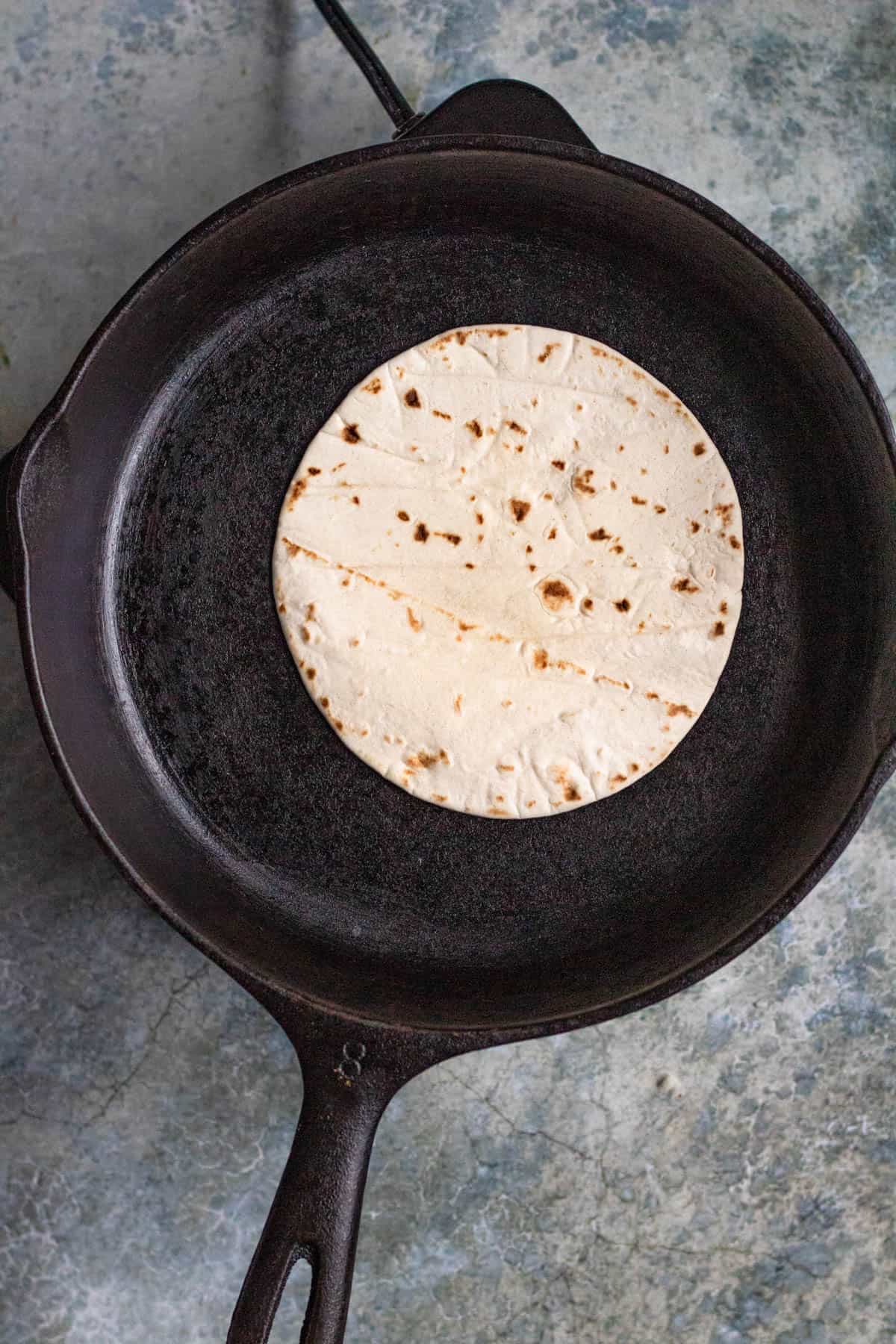 A flour tortilla warming on a cast iron skillet to make sincronizadas.