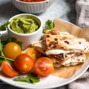 Sincronizadas cut into fours and served on a plate along with cherry tomatoes and a small bowl with guacamole.