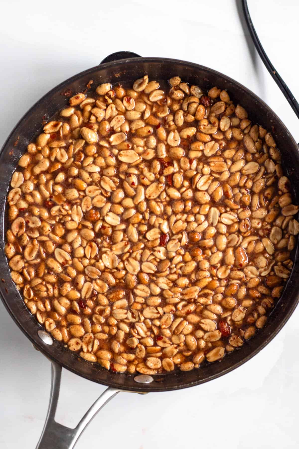 Peanuts being mixed into a glossy, spiced sugar mixture.