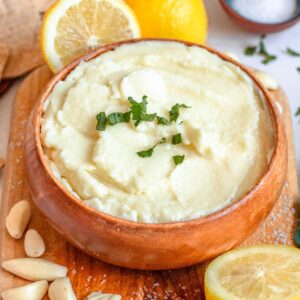 Serving bowl of Toum garnished with chopped parsley and whole garlic cloves laying around the bowl.