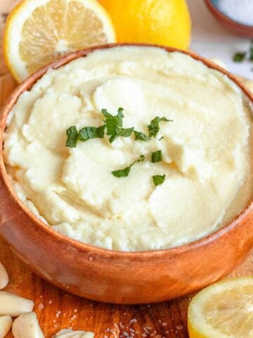Serving bowl of Toum garnished with chopped parsley and whole garlic cloves laying around the bowl.