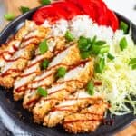 Crispy sliced Air Fryer Chicken Katsu drizzled with sauce, served with rice, shredded cabbage, and fresh tomatoes.