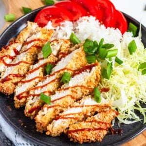 Crispy sliced Air Fryer Chicken Katsu drizzled with sauce, served with rice, shredded cabbage, and fresh tomatoes.
