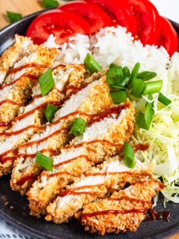 Crispy sliced Air Fryer Chicken Katsu drizzled with sauce, served with rice, shredded cabbage, and fresh tomatoes.