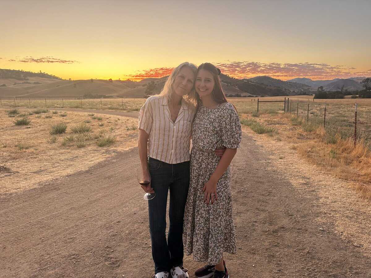 two women smiling in front of a sunset and mountains
