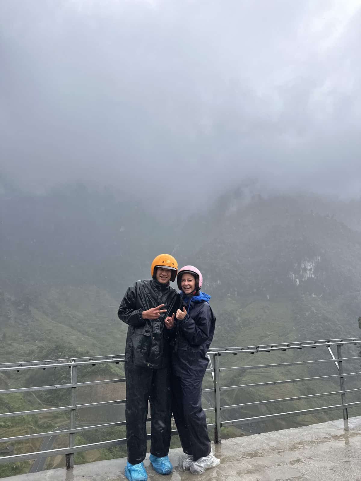 a man and woman smiling in raincoats and helmets