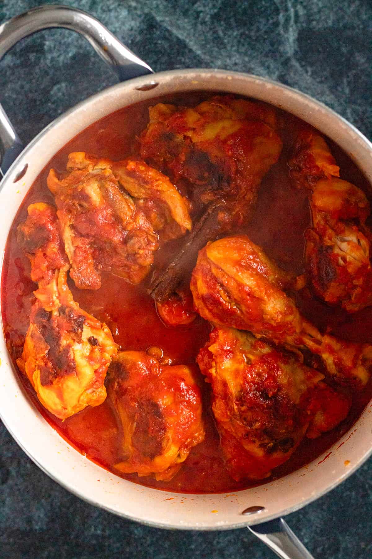 A pot of chicken simmering in crushed tomatoes, with coconut milk added, creating a creamy, rich sauce.