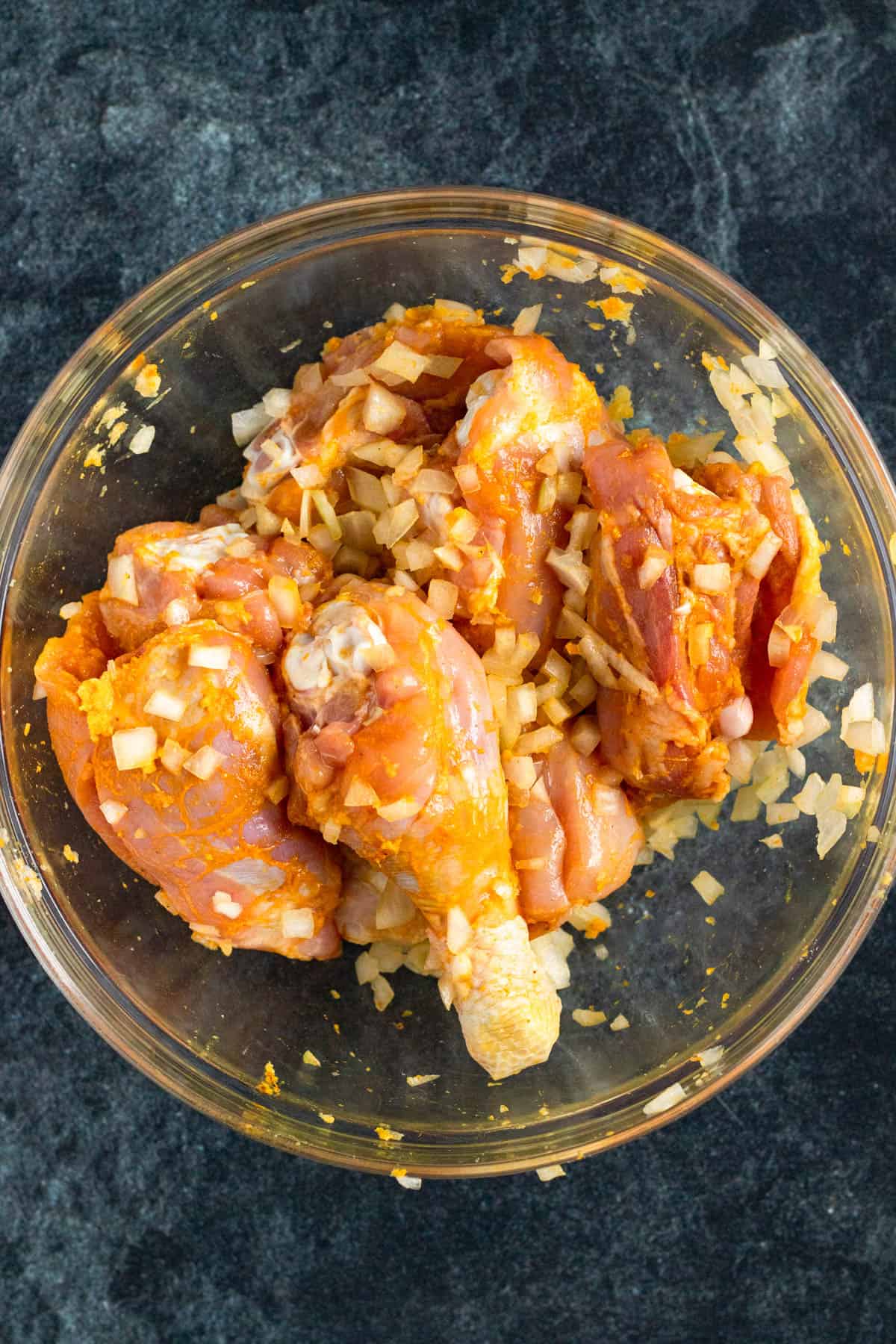 Chicken marinating in a bowl with ginger, garlic, turmeric, and sliced onions.
