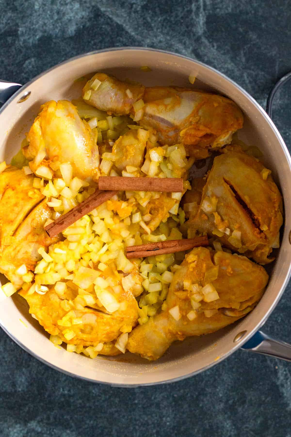 Cinnamon sticks added to a pot of browning chicken.