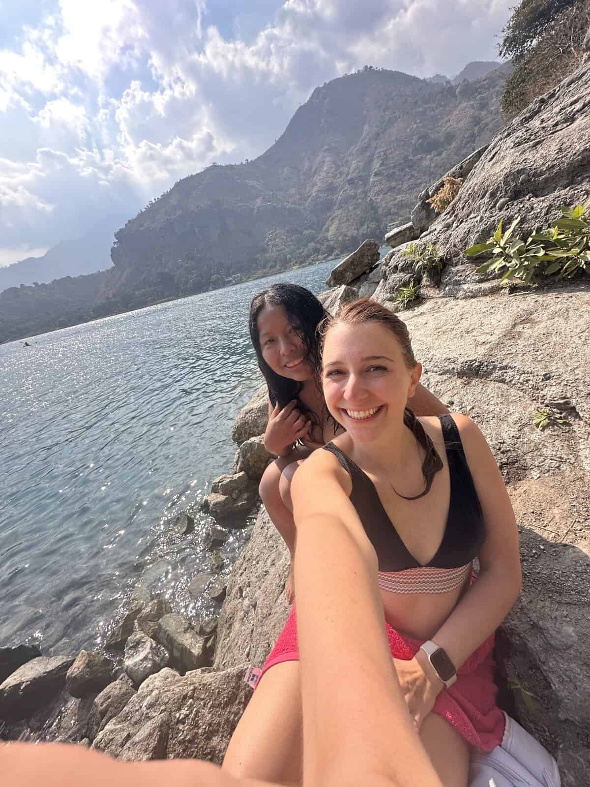 Two girls in swimsuits smiling in front of a lake