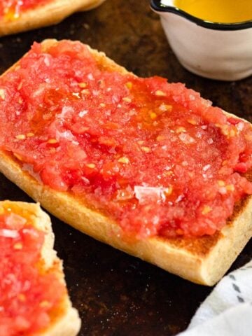 Pan con Tomate arranged on a baking sheet with a small measuring cup of oil.