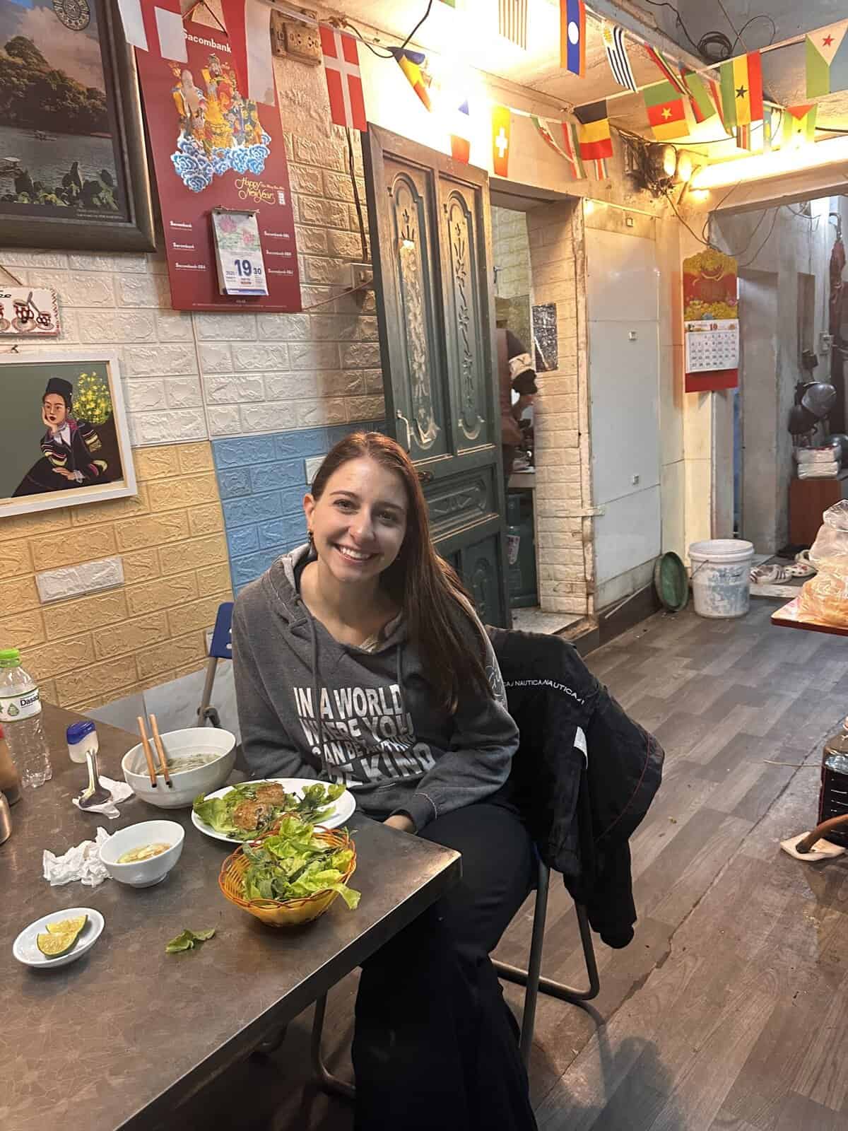 A girl sitting at a table in the restaurant with spring rolls in front of her.