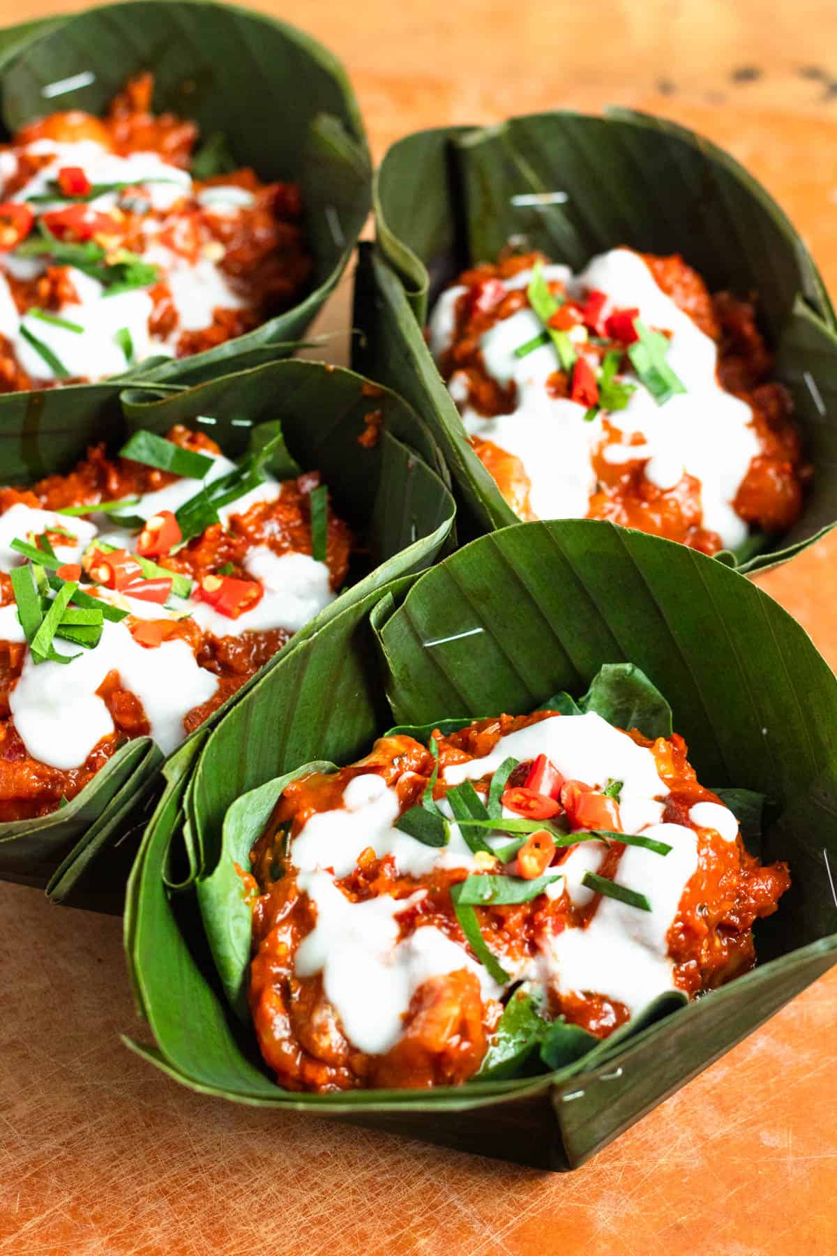 Banana leaf bowls filled with amok curry, topped with coconut milk, sliced chili peppers, and lime leaves.