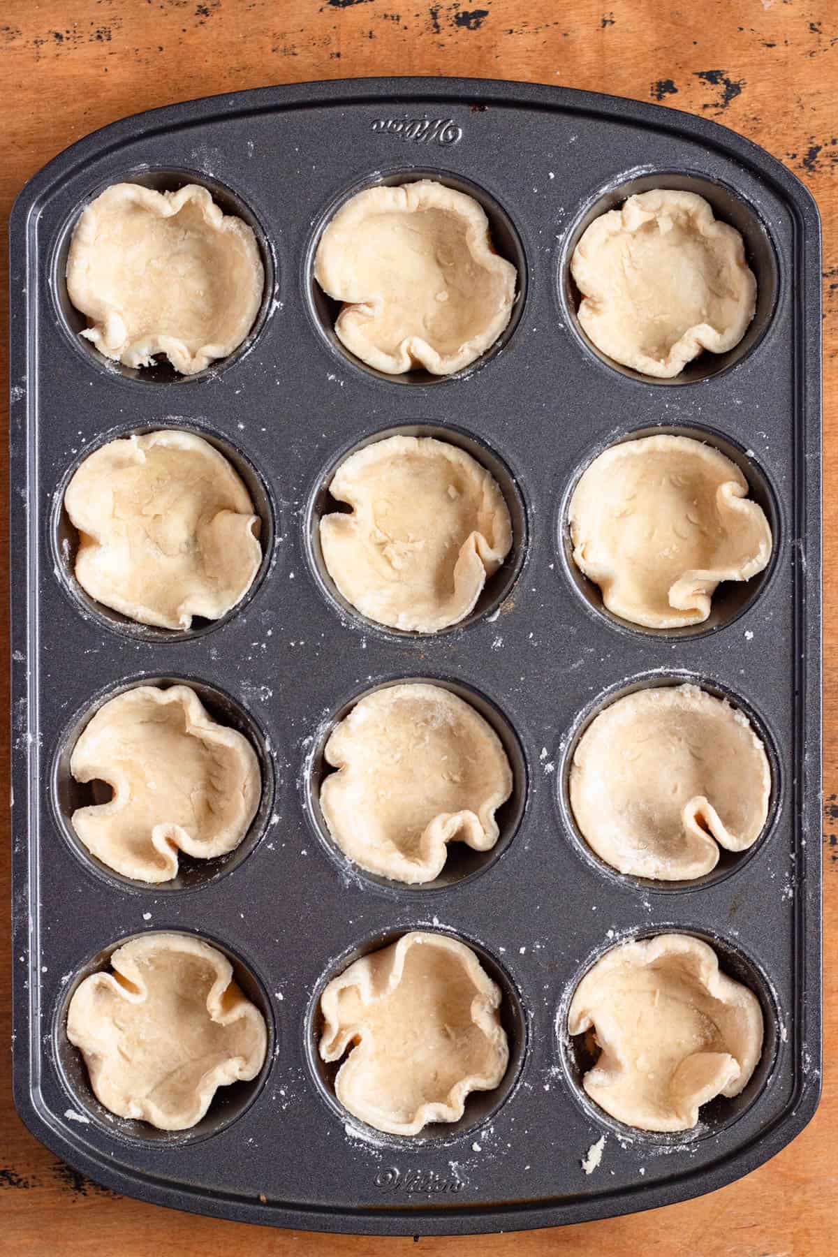 Dough circles carefully placed into the cups of a muffin pan.