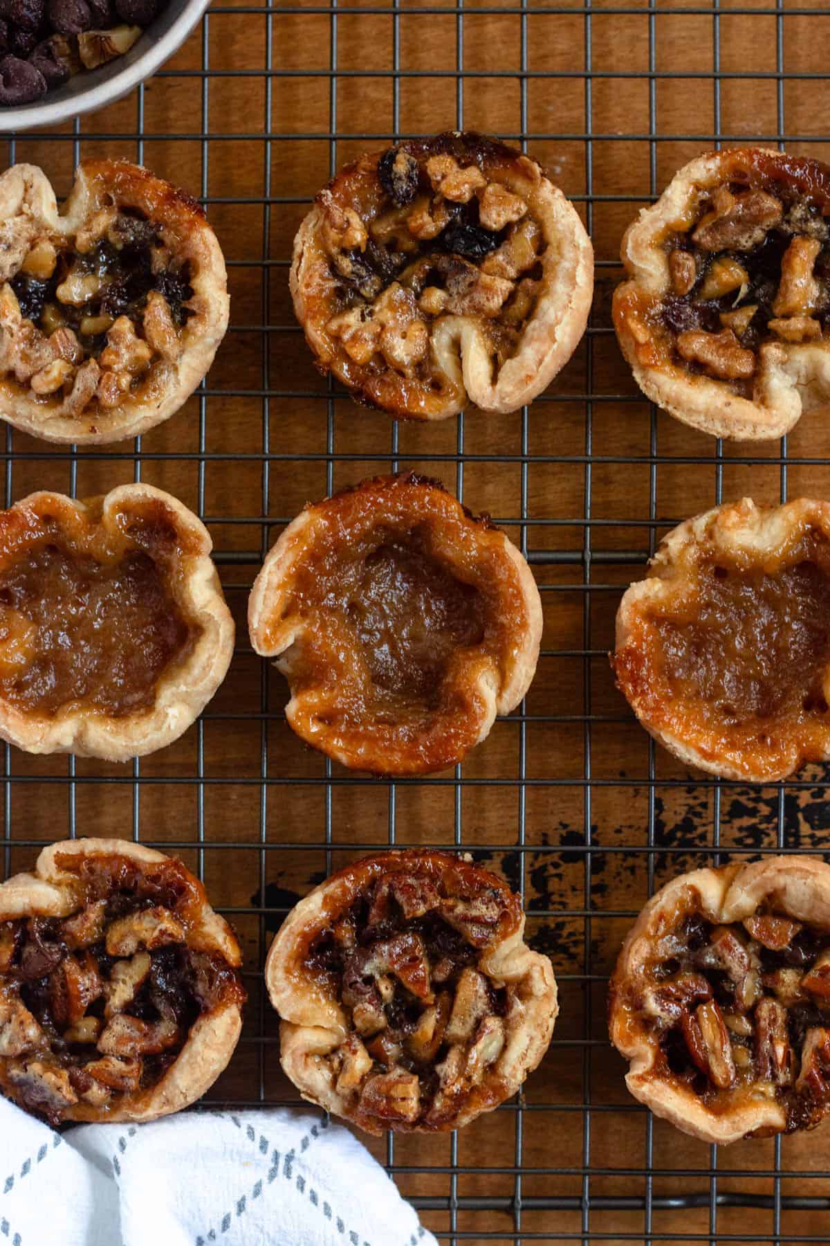 Close-up image of assorted Authentic Canadian Butter Tarts with plain and nut fillings on a cooling rack.