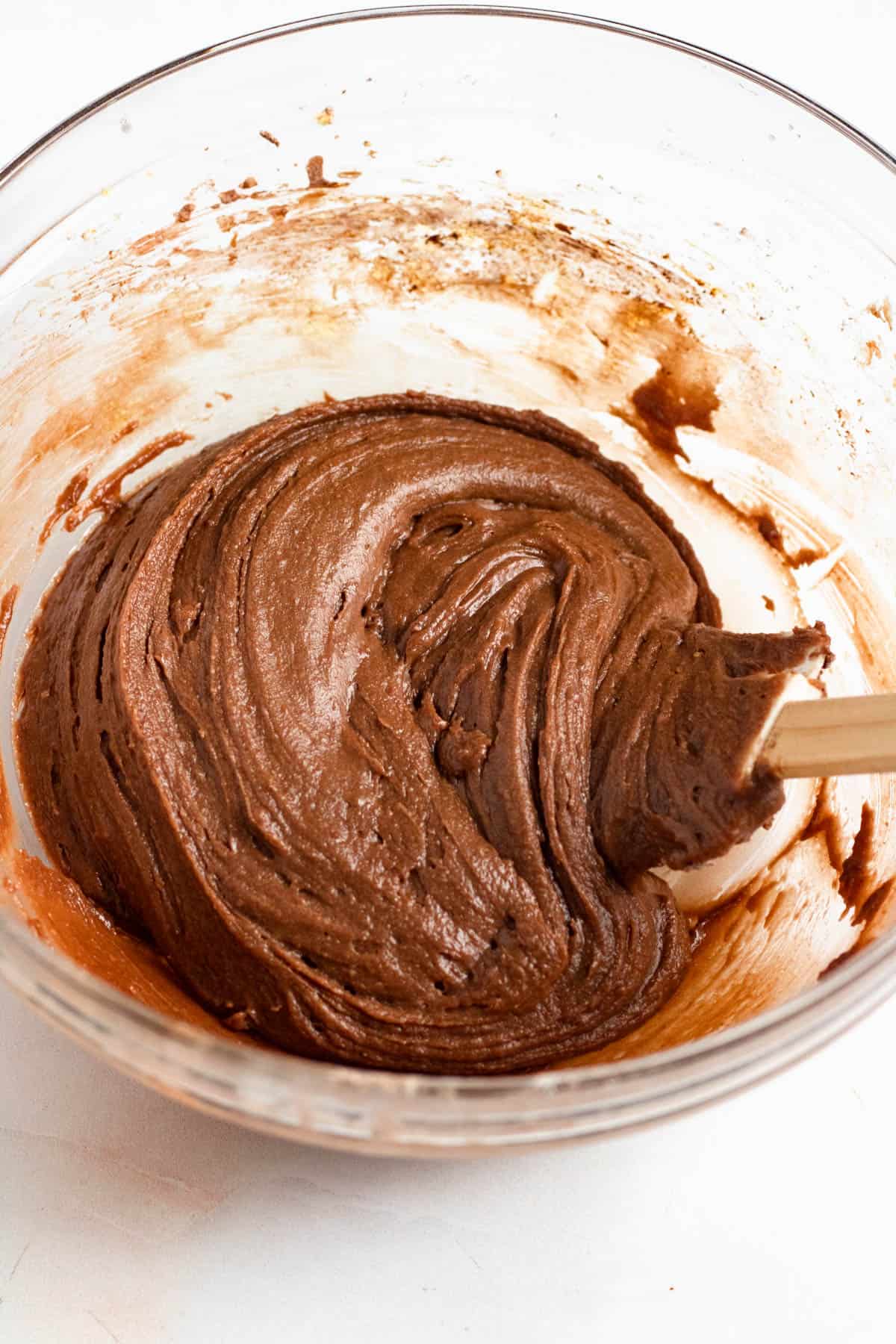 Chocolate Pizzelle batter being mixed in a bowl with eggs, sugar, butter, vanilla, flour, baking powder, and cocoa powder.
