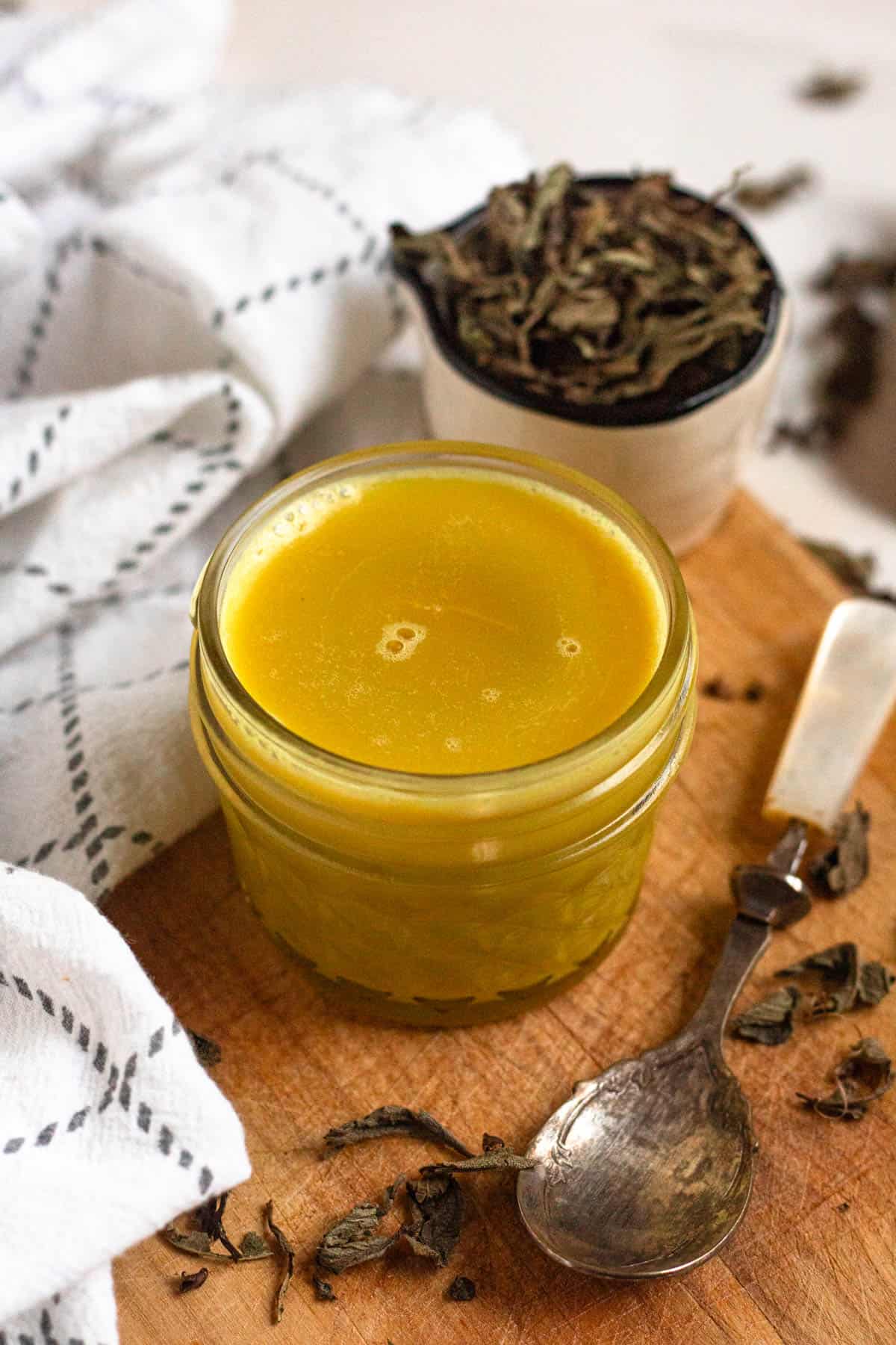A small jar of golden Niter Kibbeh set on a wooden board with a spoon.