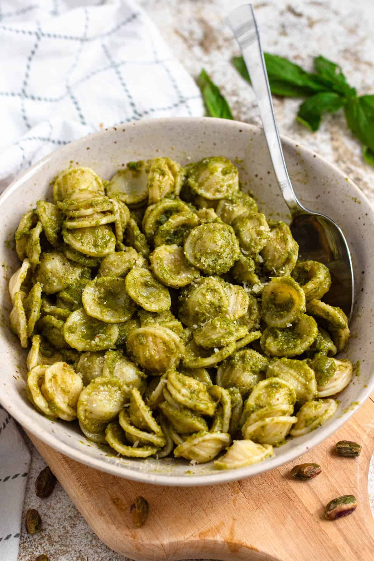 Bowl of pasta coated in green pesto sauce with a spoon.