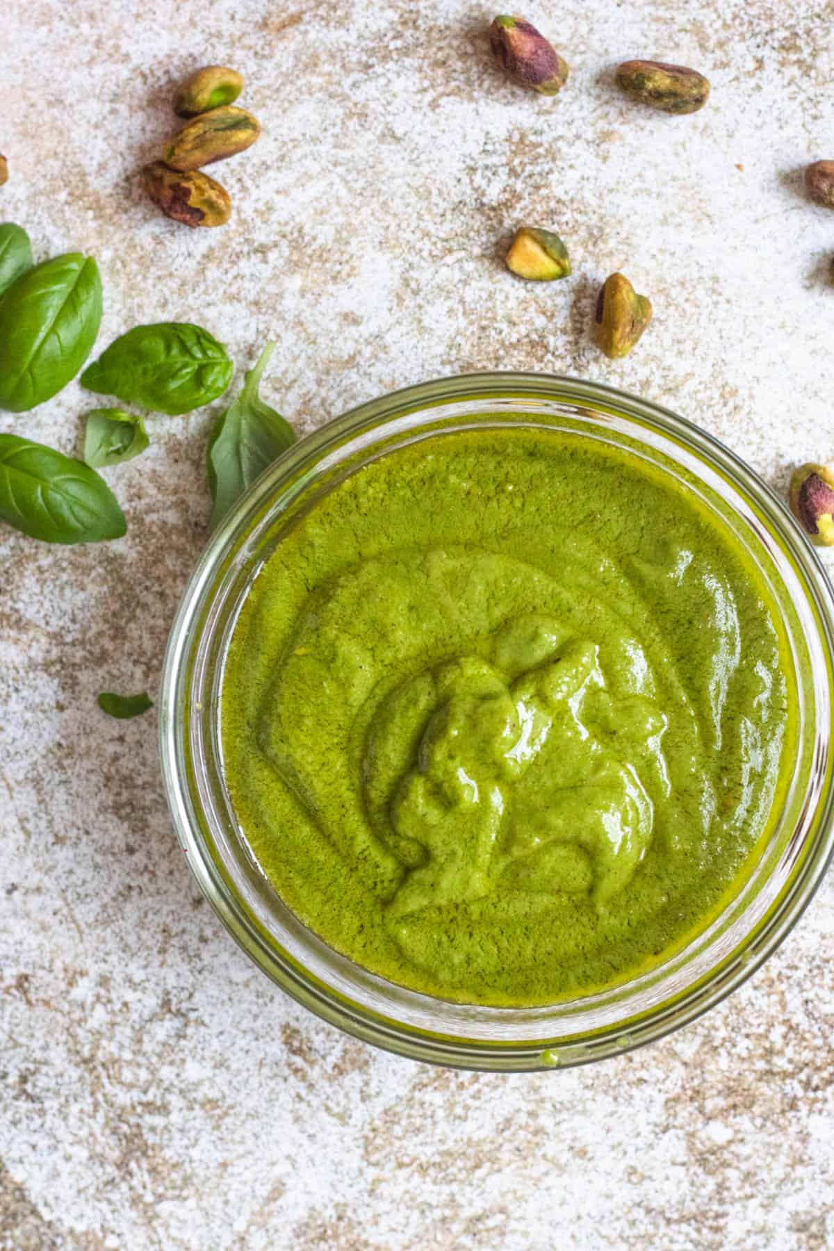 Bowl of Pistachio Pesto with basil leaves and pistachios near it.
