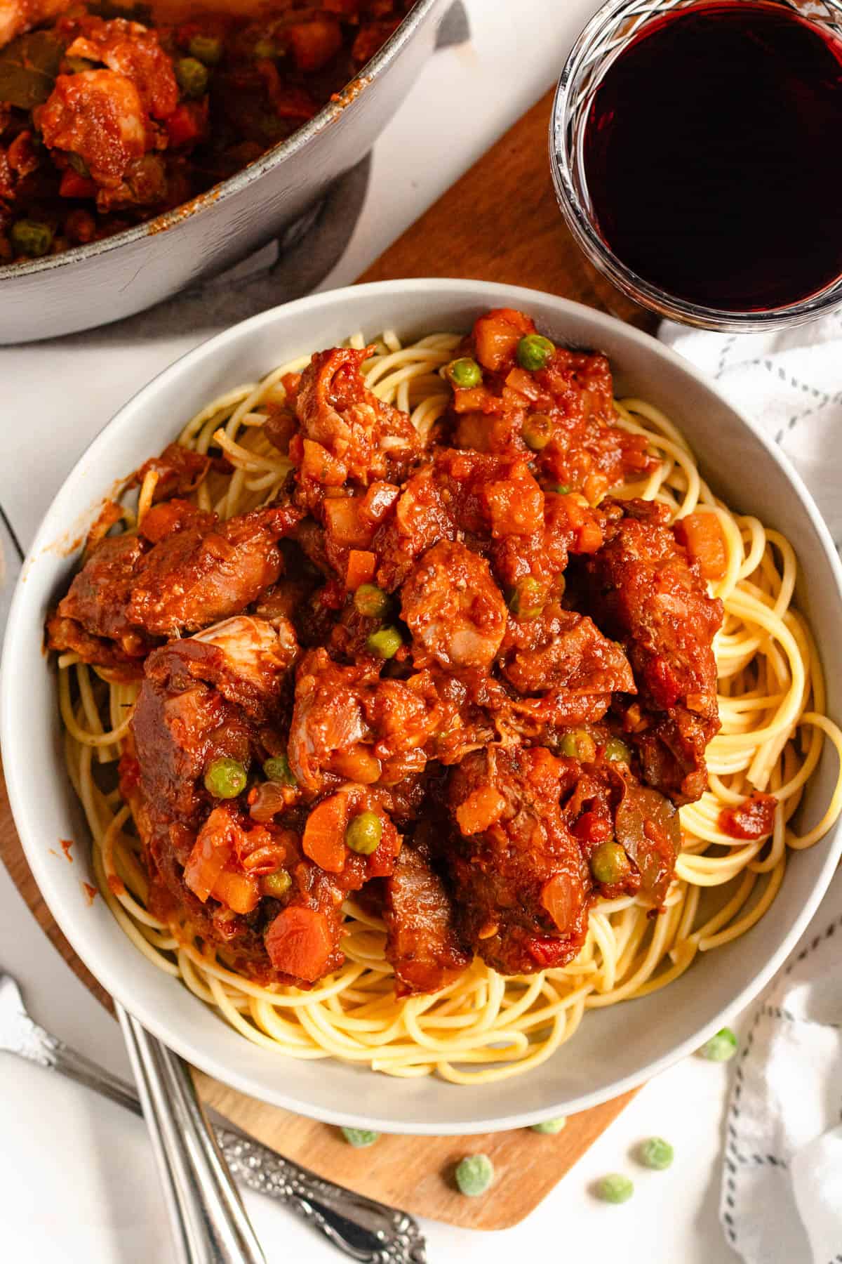 Top image of hearty Rabbit Stew with carrots, and peas served over a bowl of spaghetti.
