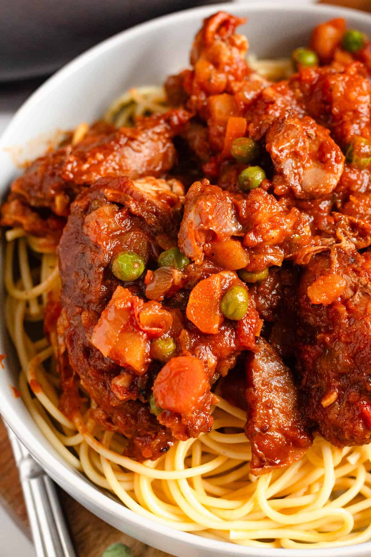 Close-up image of hearty Rabbit Stew with carrots, and peas served over a bowl of spaghetti.