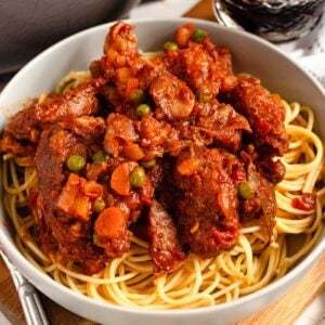 Hearty Rabbit Stew with tender meat, carrots, and peas served over a bowl of spaghetti.