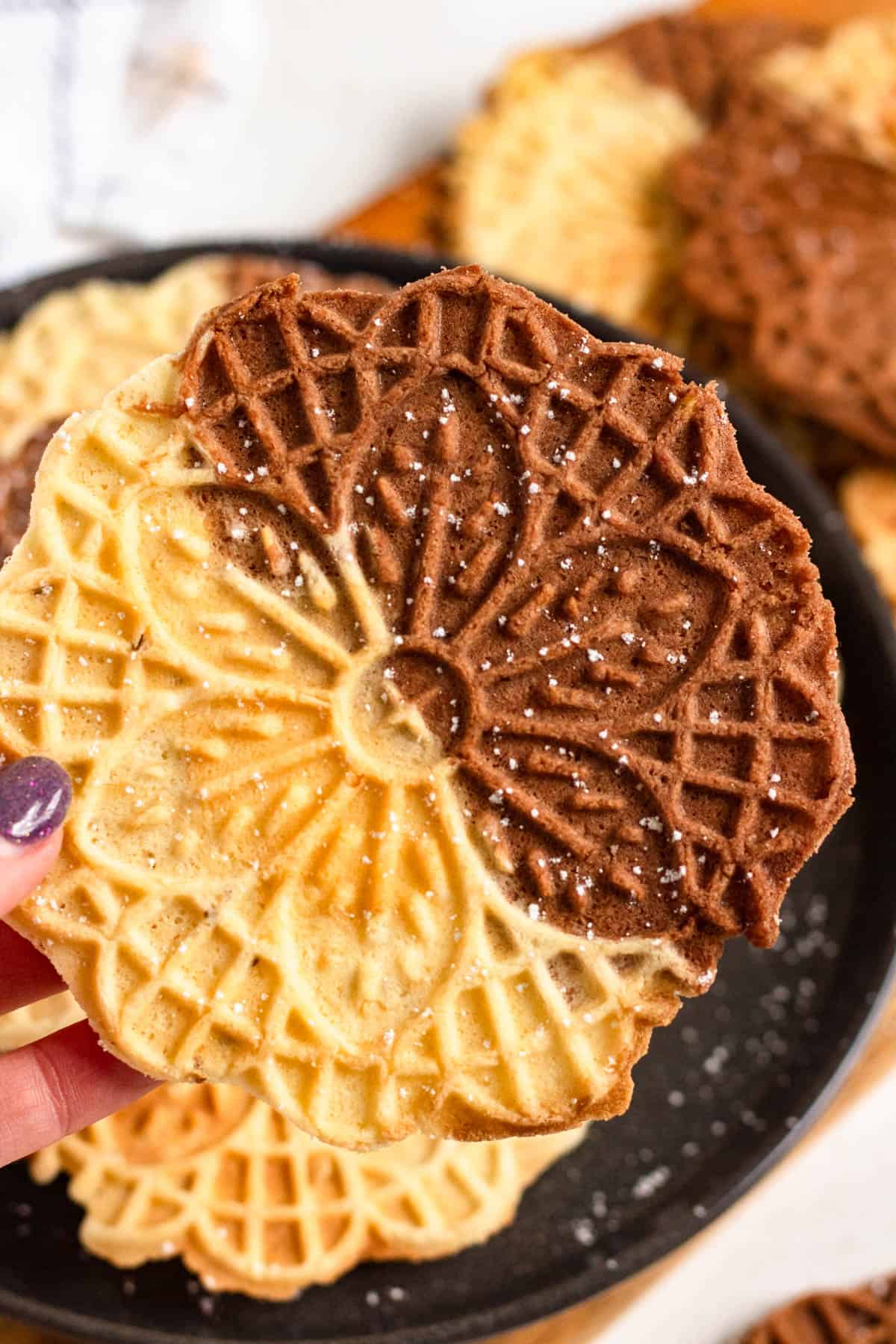 Hand holding a Chocolate and Vanilla Swirl Pizzelle cookie with a delicate lace pattern.