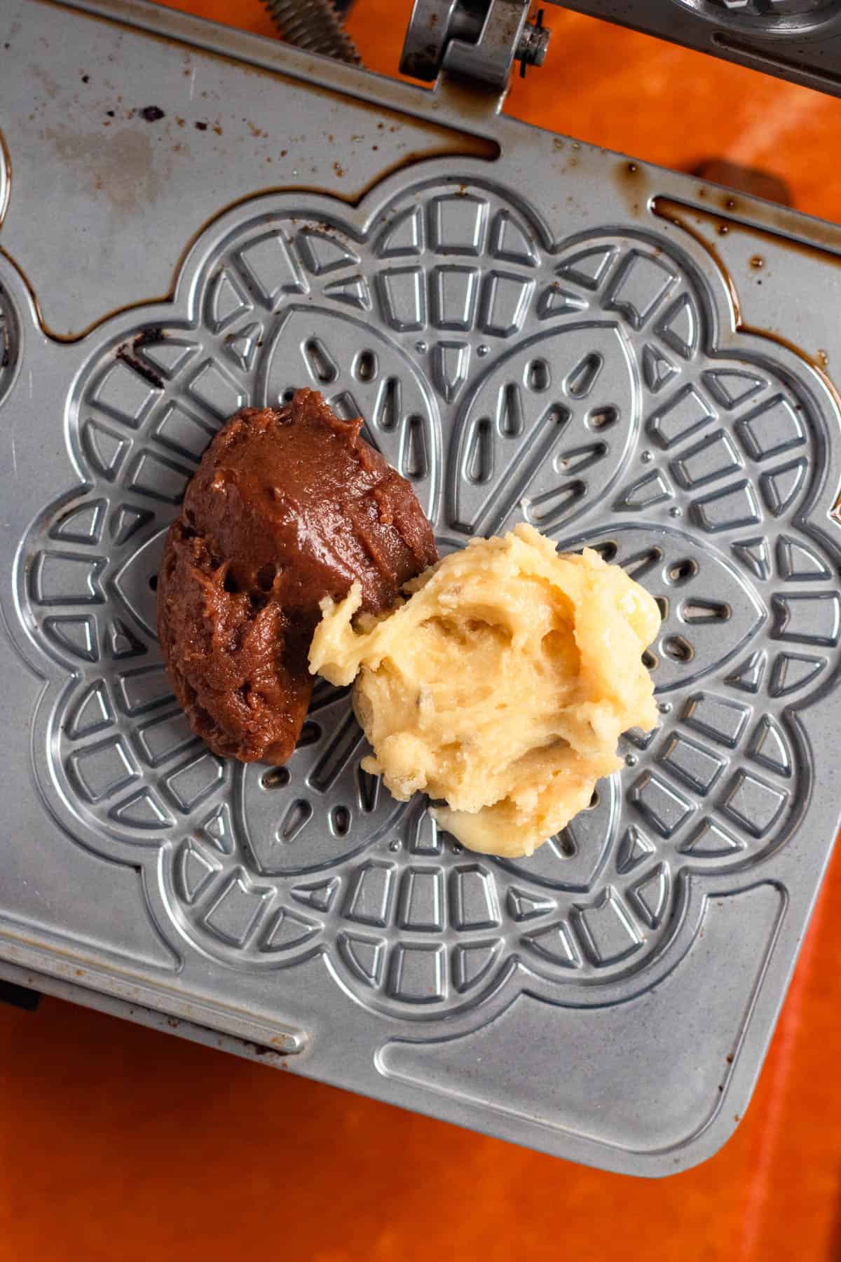 Vanilla and Chocolate Pizzelle batter dropped onto the center of a pizzelle iron to create a swirl cookie.