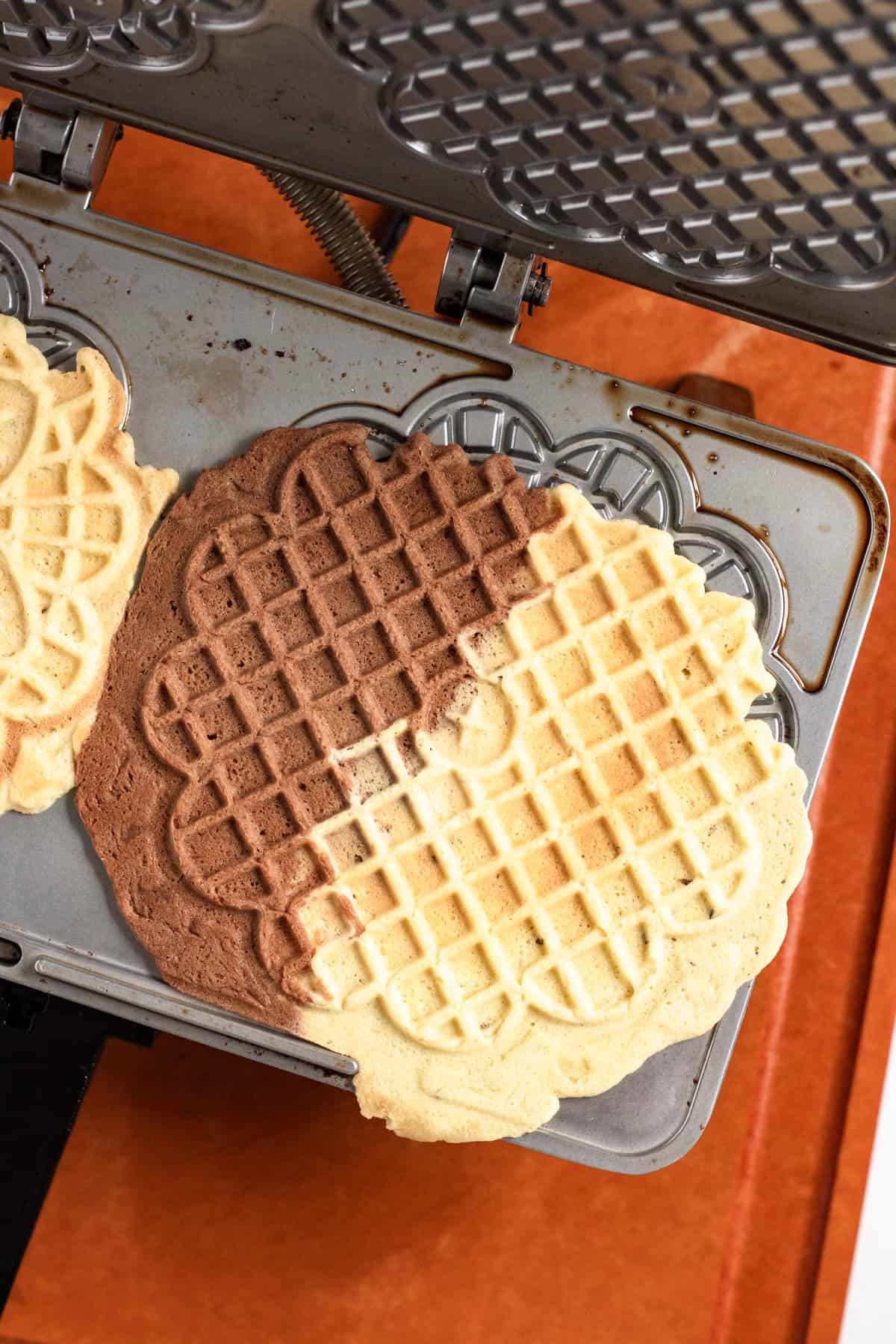 Chocolate and Vanilla Swirl Pizzelle cookies cooked in a pizzelle maker.