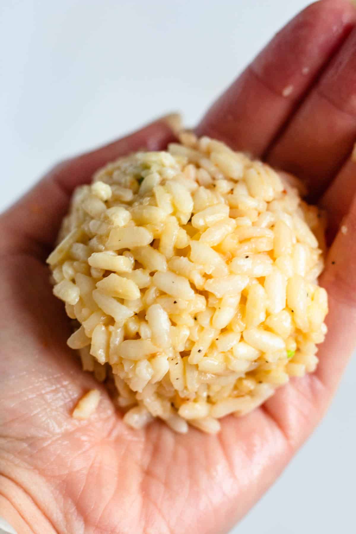 Cooked rice shaped into a compact ball in a hand.