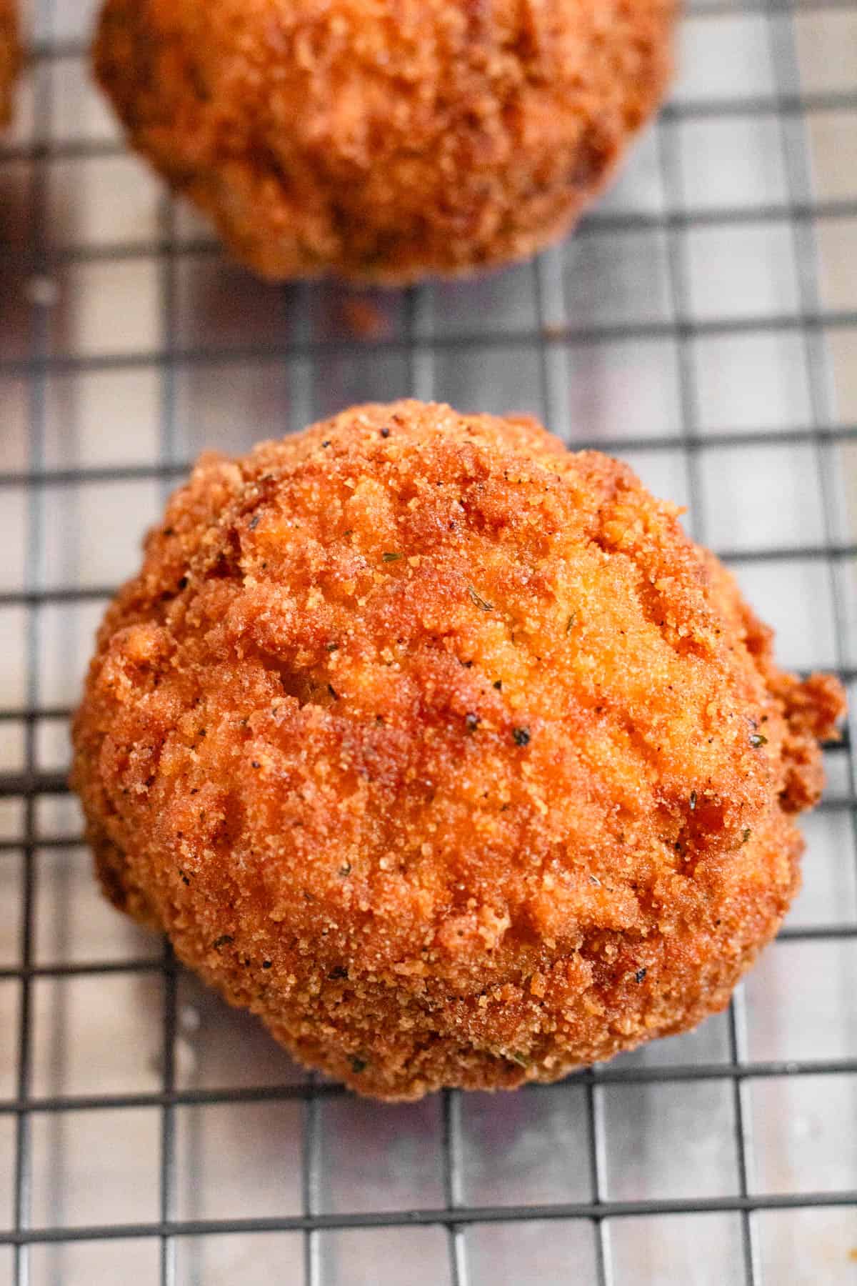 Golden fried Arancini cooling on a wire rack.