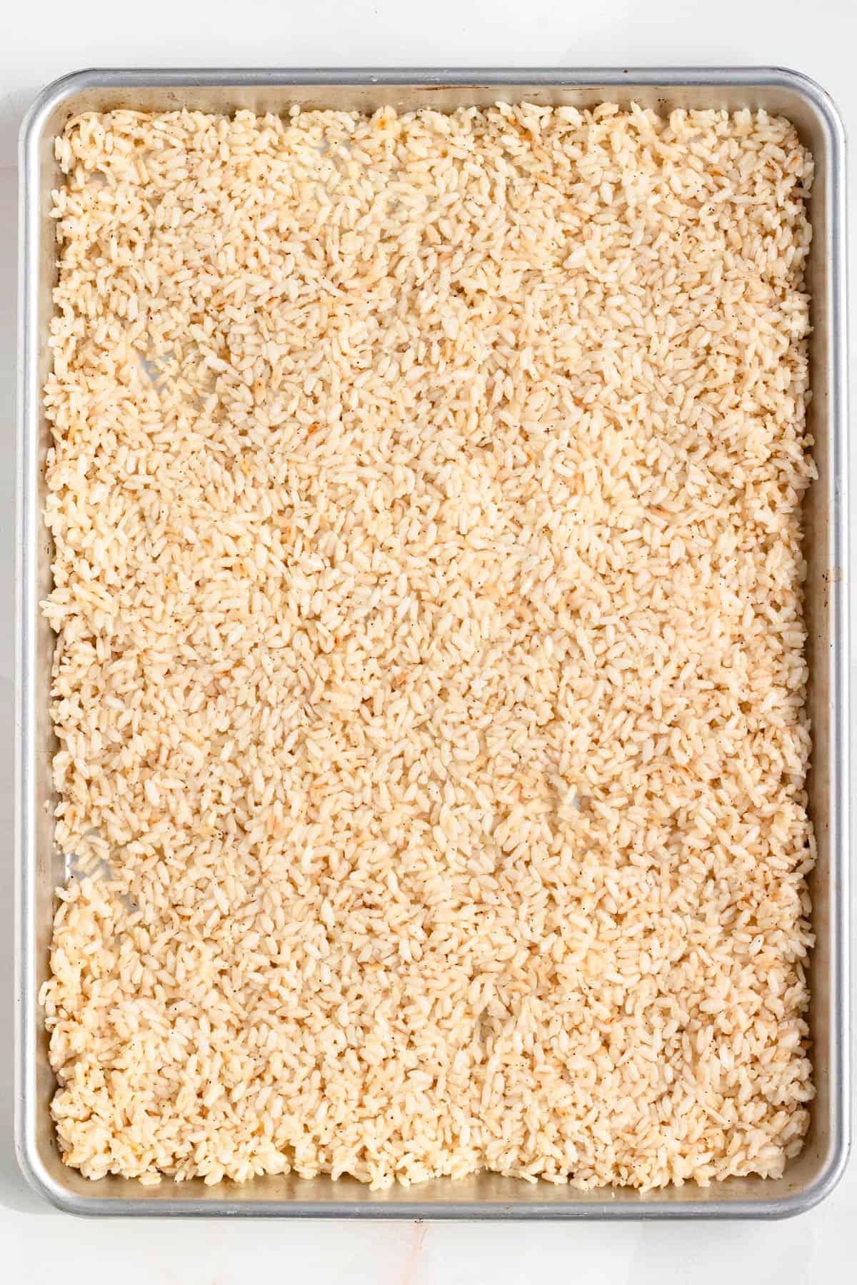Cooked rice spread out on a baking sheet.