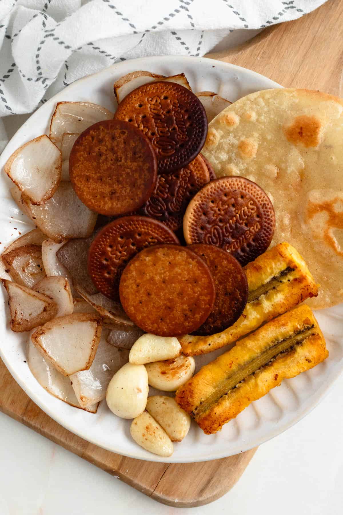 Plate of toasted mole ingredients including onion, garlic, plantain, tortilla, and galletas Marias.