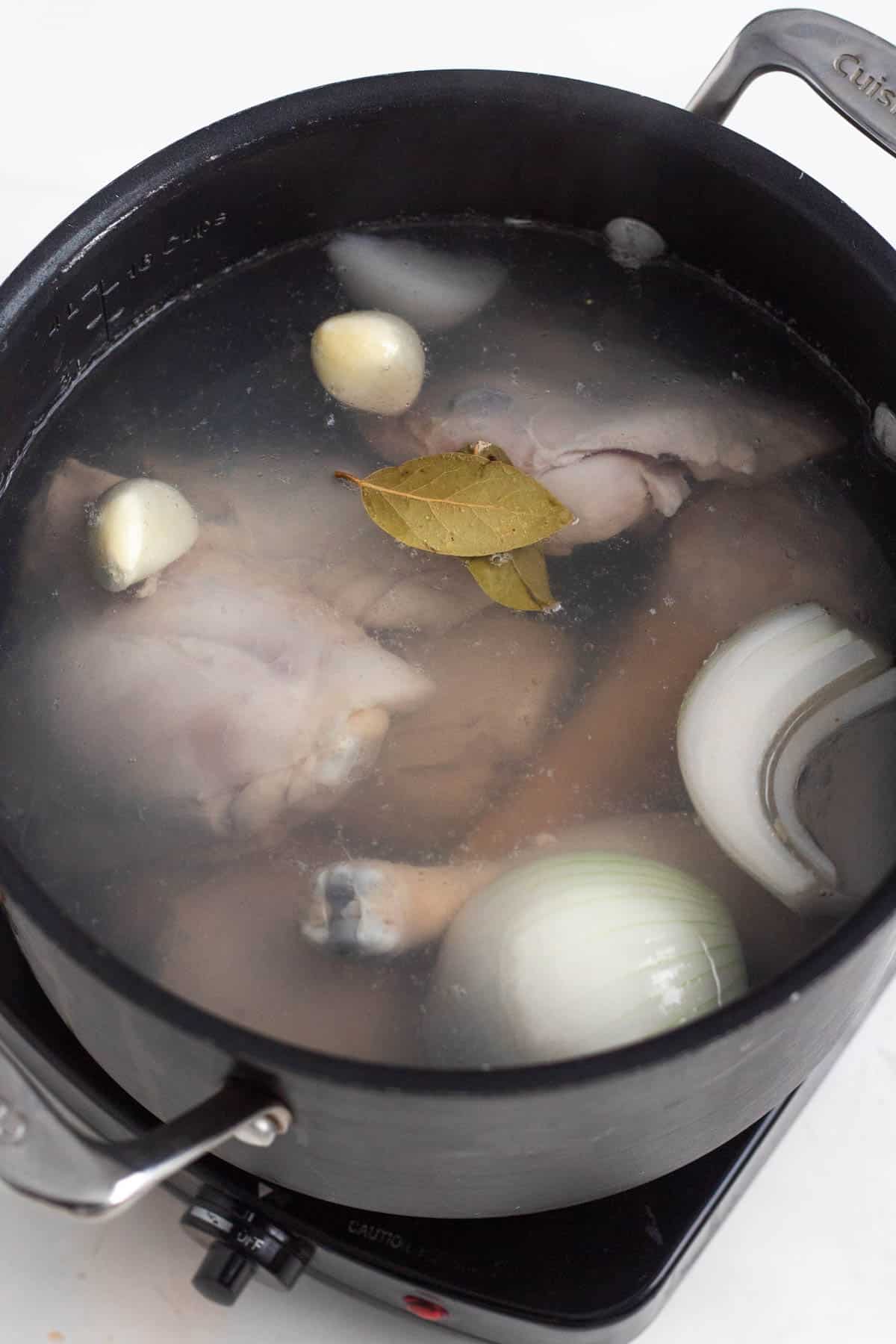 Chicken simmering in a pot with onion, garlic, and bay leaves.