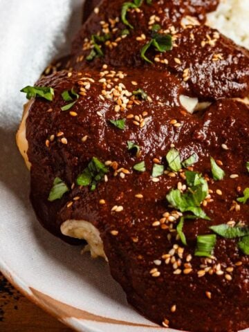 Chicken in mole poblano sauce topped with sesame seeds and herbs, served with rice.