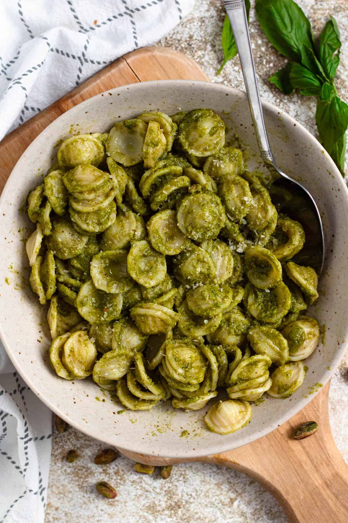 Bowl of pasta coated in green pesto sauce with a spoon.
