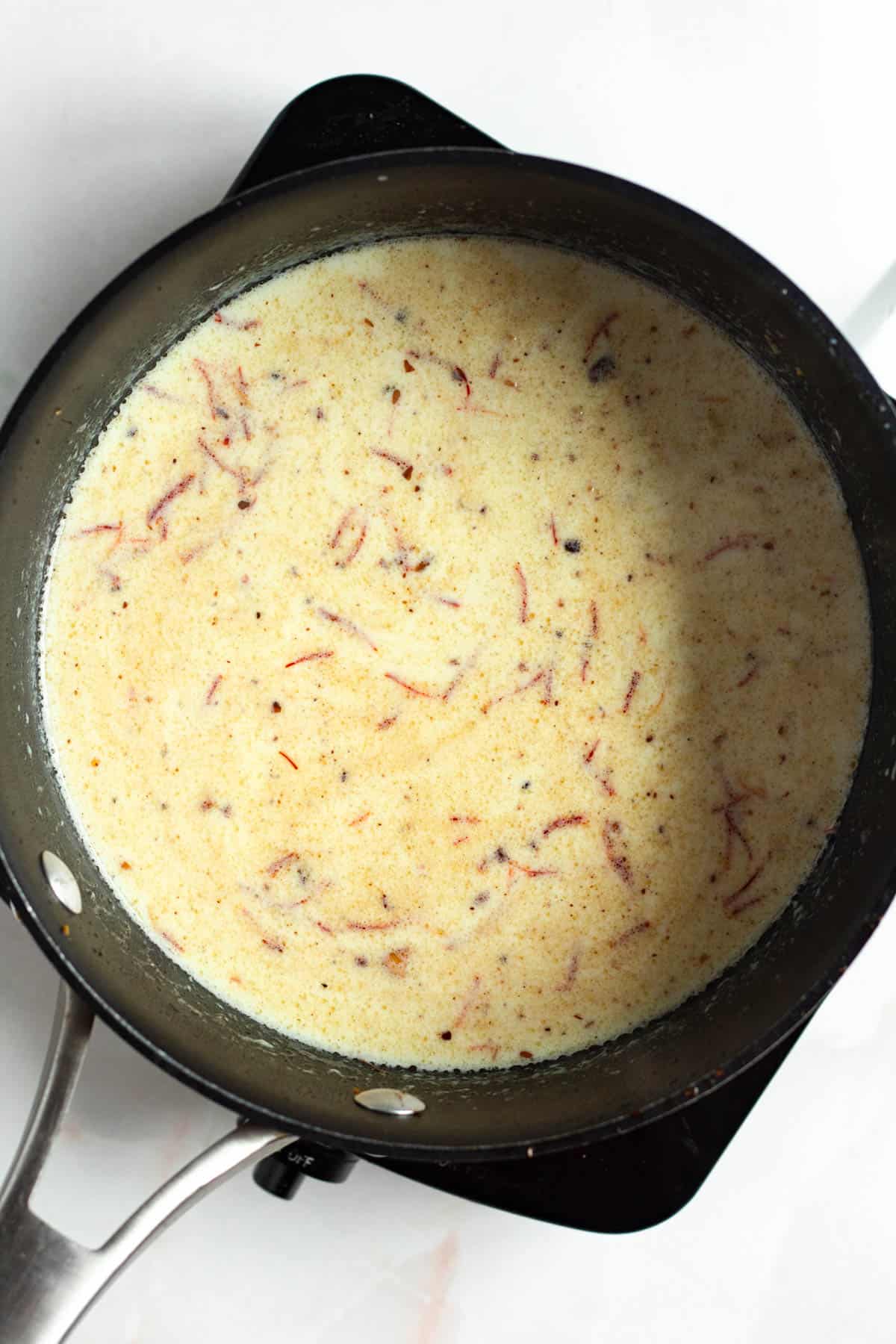 Creamy milk simmering in a pot with saffron threads and spices.