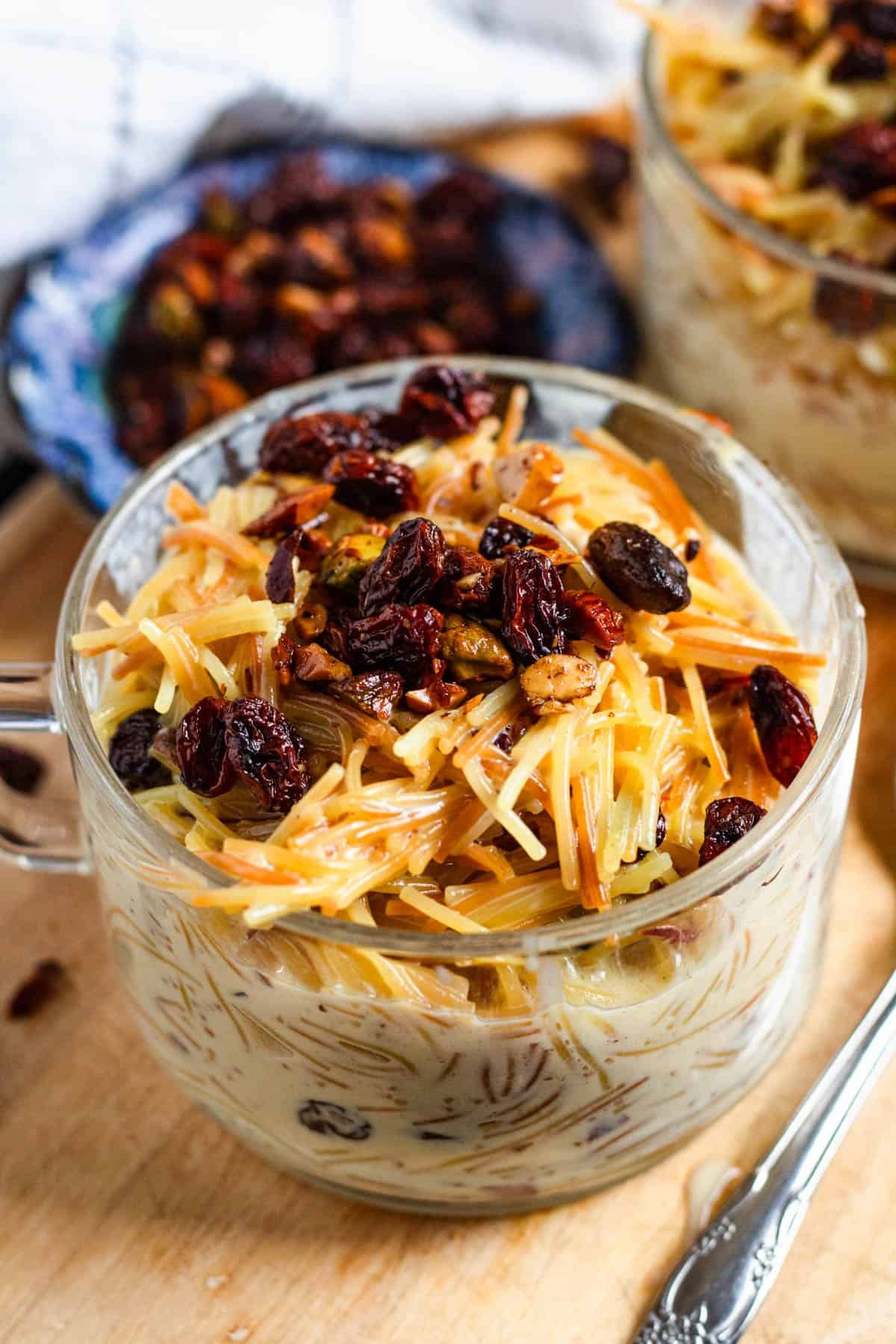 A glass bowl of warm vermicelli porridge topped with toasted nuts and raisins.