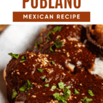 Pinterest image of a close-up shot of a plate of chicken in mole poblano sauce topped with sesame seeds and herbs, served with rice.