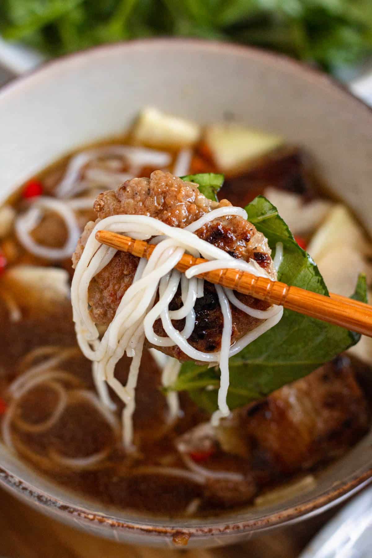 Close-up of flavorful Bún Chả with juicy grilled pork, rice noodles, herbs, and dipping sauce held with chopsticks.