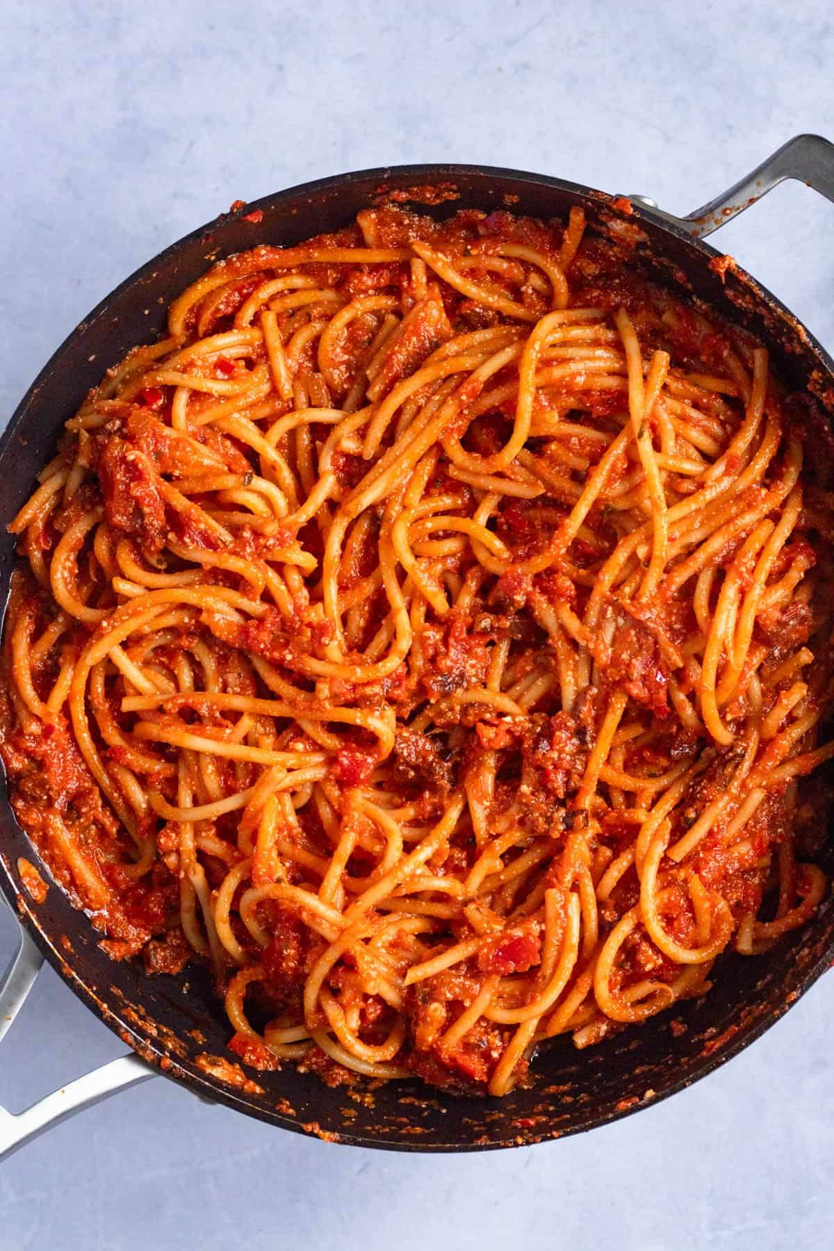 Cooked bucatini added to the Amatriciana sauce in a pan.