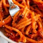Bucatini all’Amatriciana with crispy guanciale and rich tomato sauce on a fork.