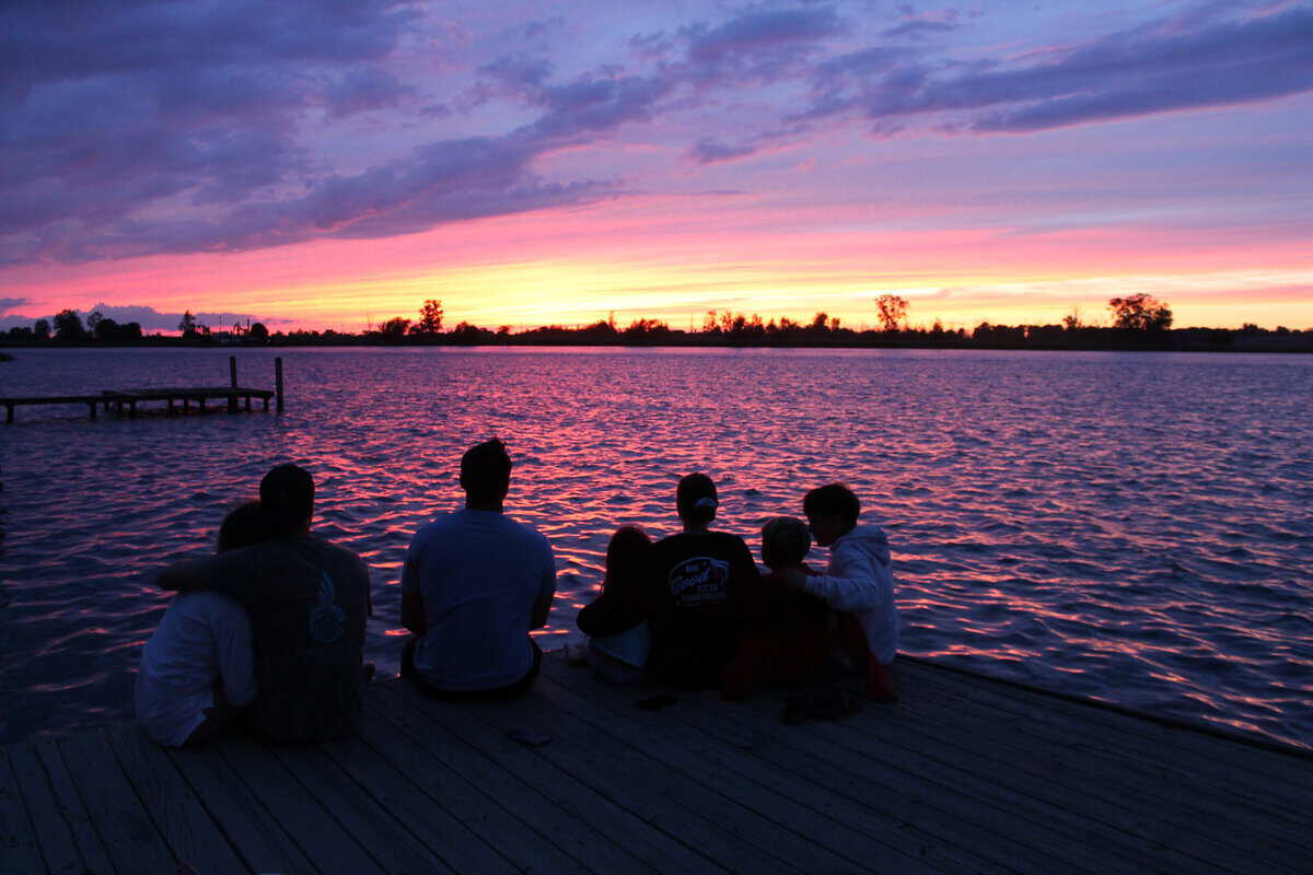 7 cousins watching the sunset together in front of water. 