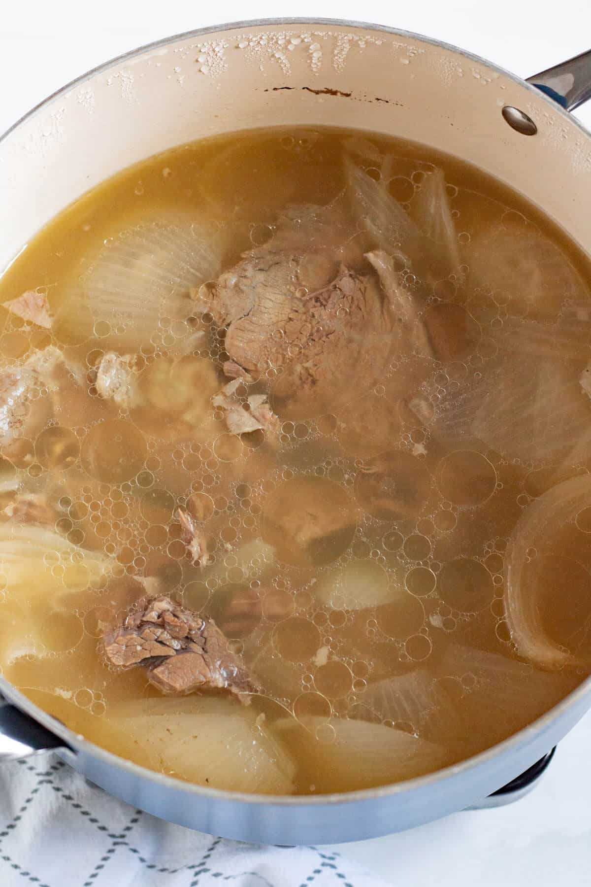 Beef, onion, and spices simmering in a pot to make flavorful stock for bitterballen.