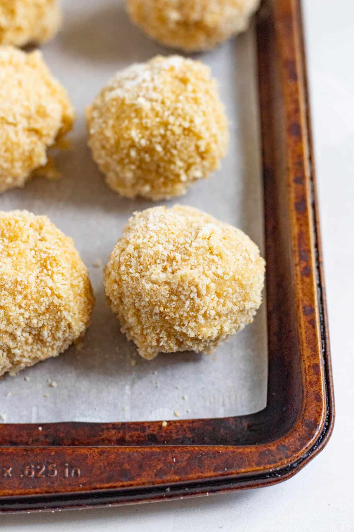 Small bitterballen balls arranged on a baking sheet before frying.