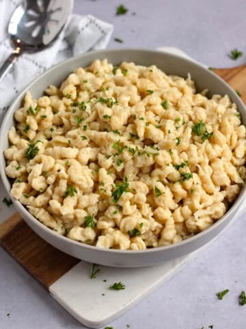 Homemade German spaetzle tossed with butter and fresh parsley in a serving bowl.